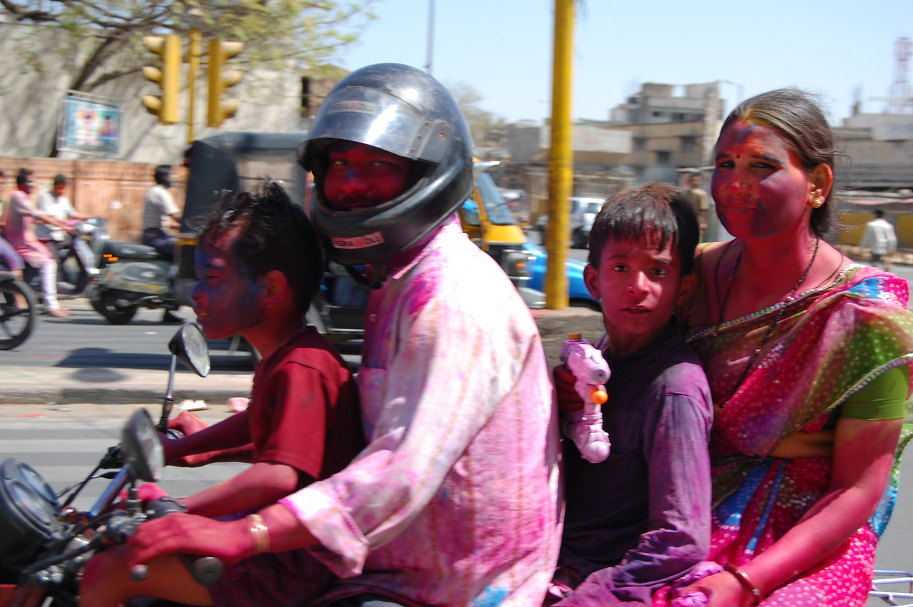 A colorful family rides a motorbike toward the end of Holi in India