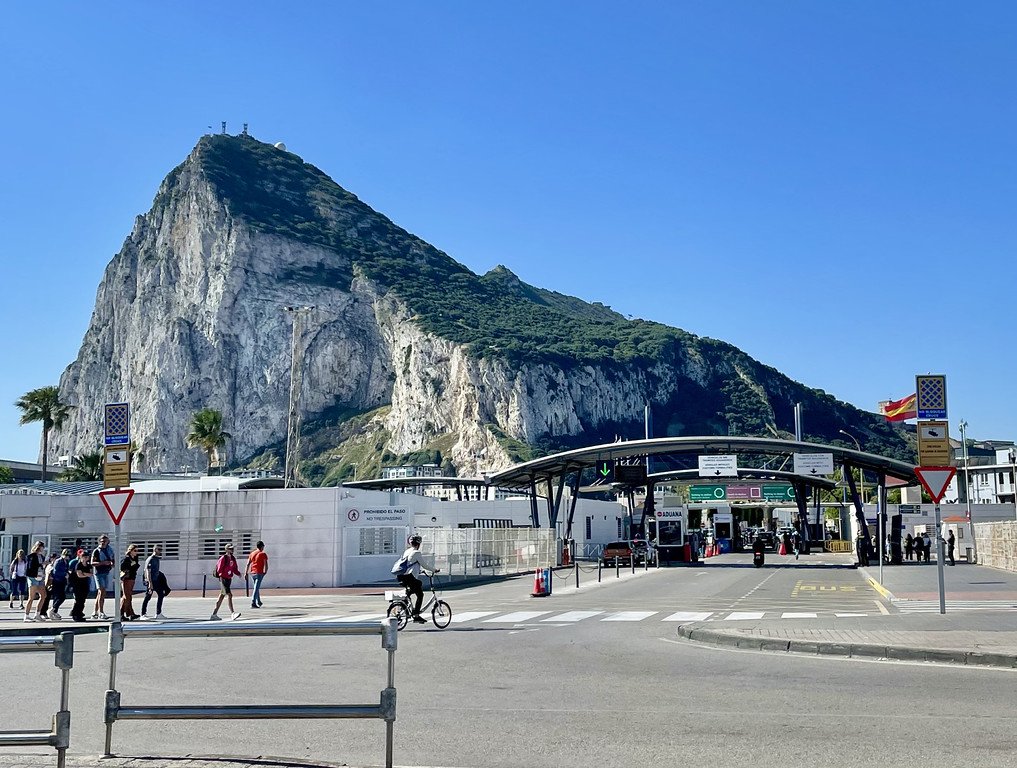 Pedestrian border crossing into Gibraltar showing a passport control booth on the right and the Rock of Gibraltar in the background.