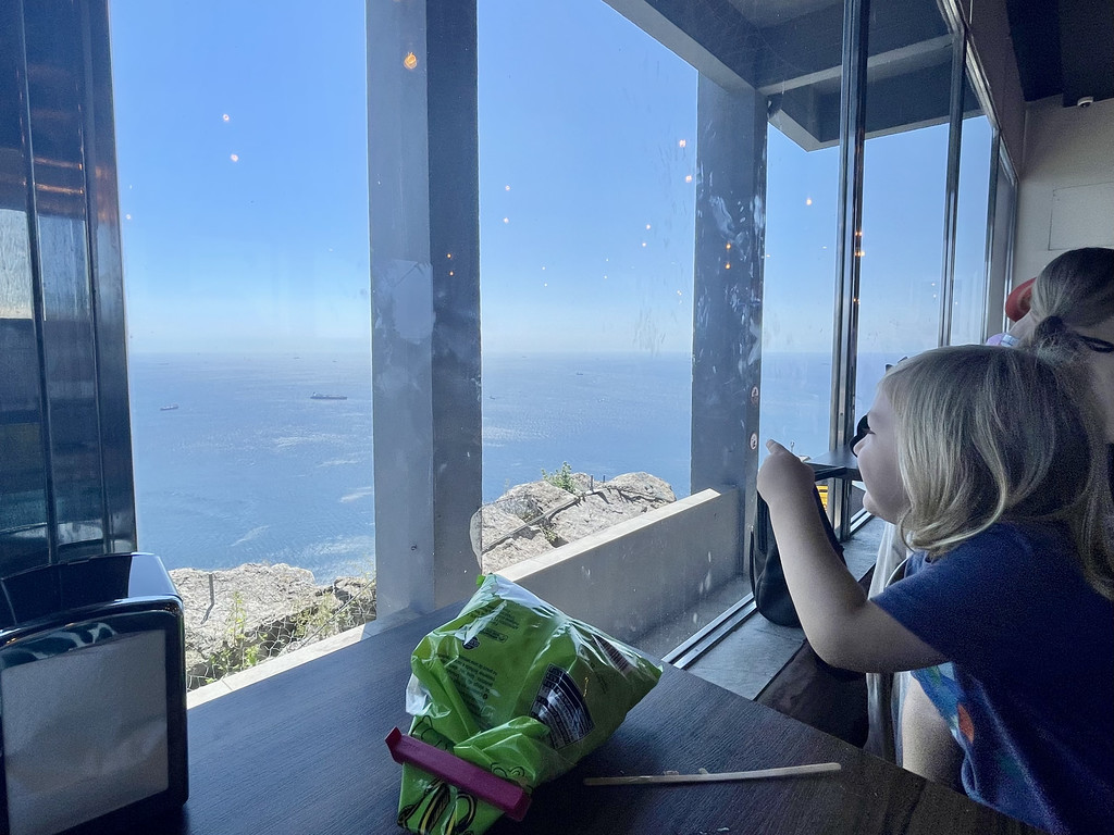 A child looking out the Top of the World Café window on the Rock of Gibraltar toward the water and boats below.