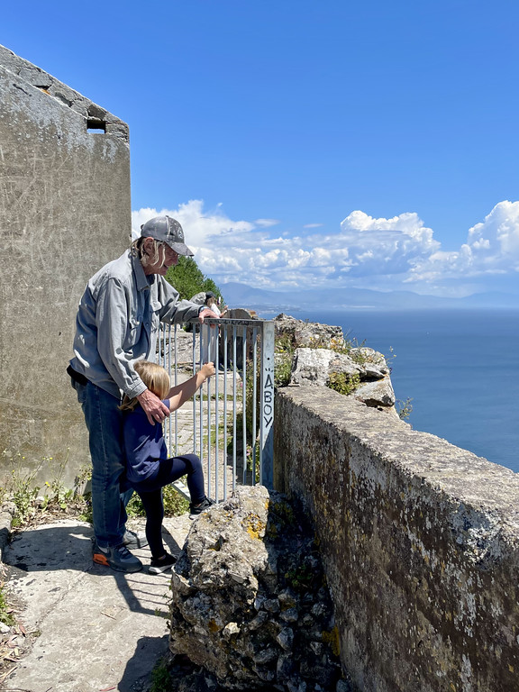 An adult and a child standing at a metal railing along the fortifications on the Rock of Gibraltar, overlooking a rocky drop-off.