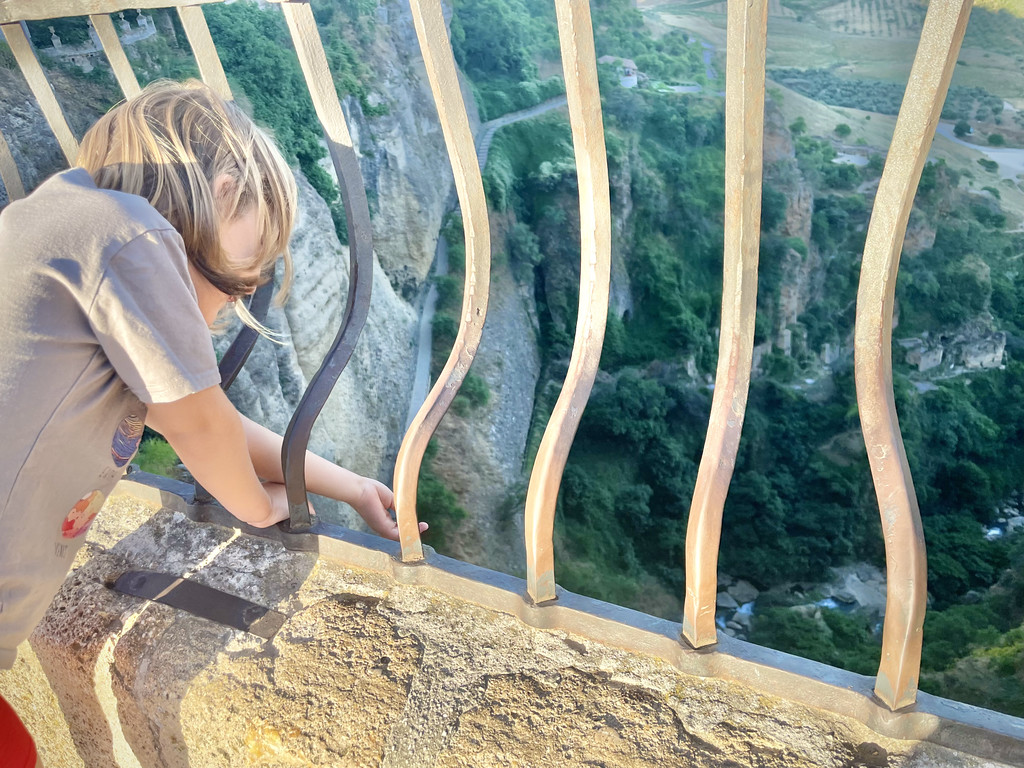 A child leaning into curved metal safety railings, looking down over El Tajo gorge in Ronda.