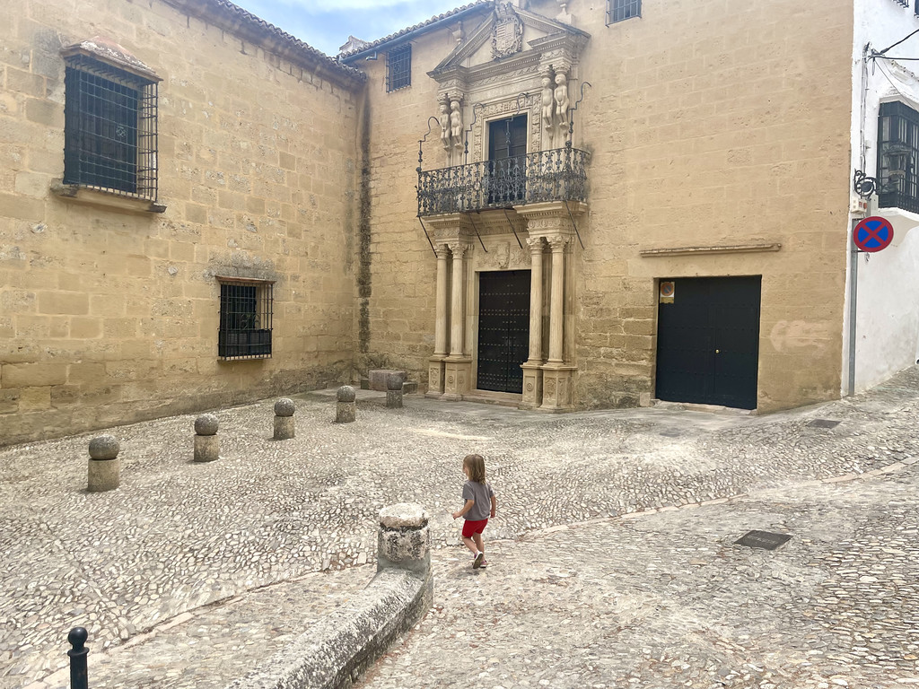 A child running across a cobblestone plaza in front of a large historic stone building in Ronda.