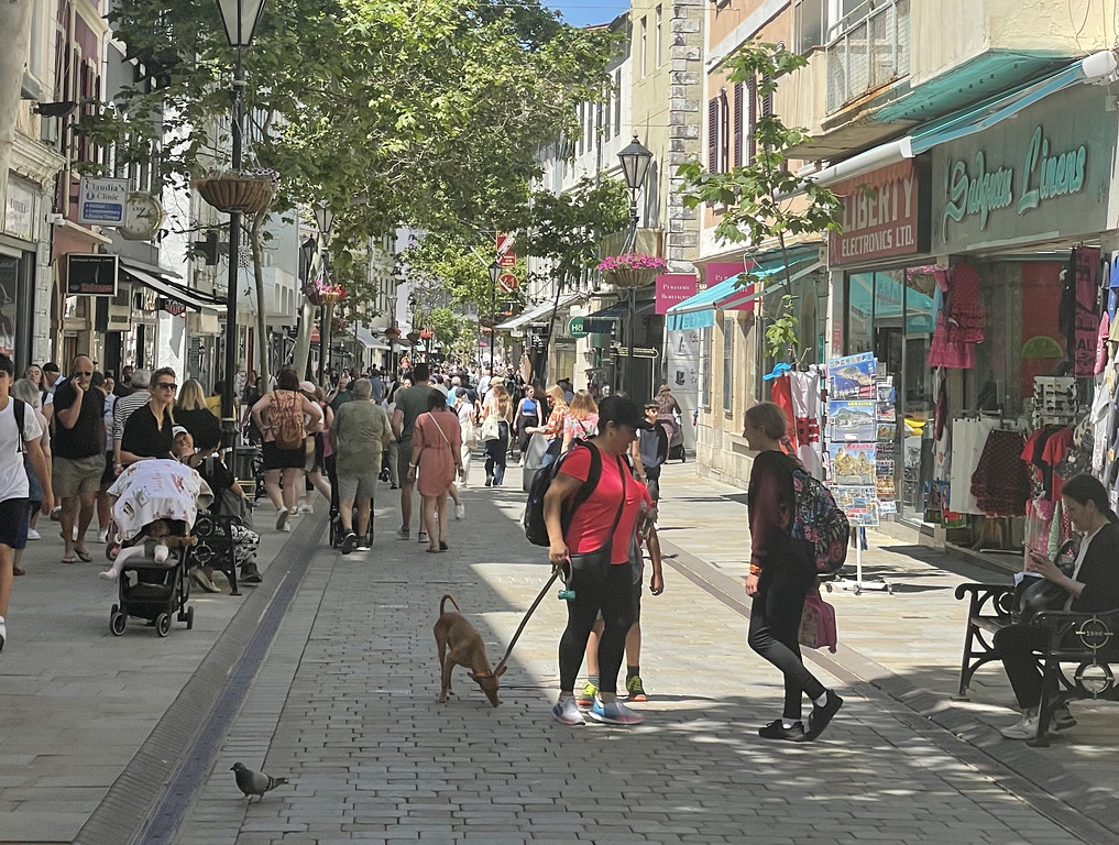 A crowded shopping street in Gibraltar with shaded sidewalks and storefronts.