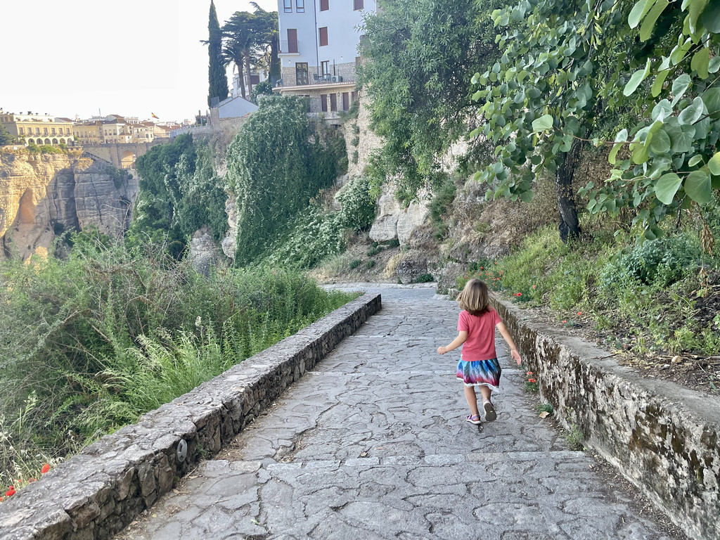 A child walking down a stone garden pathway with Ronda's old town visible in the background.