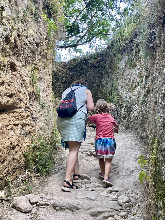 An adult and a child holding hands while walking on a rocky gorge trail between stone walls.